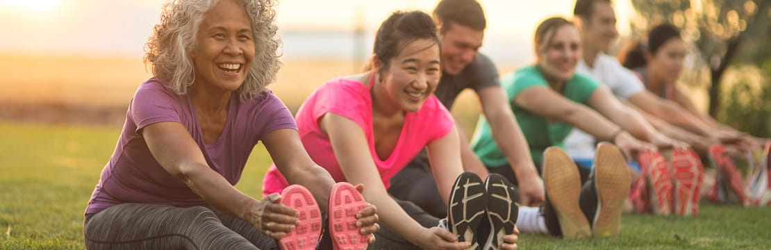 A row of smiling individuals stretching as part of their workout